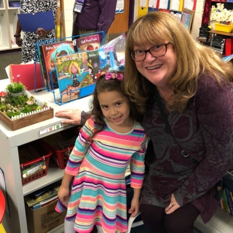 Mary posing for a photo with a young student in a striped dress